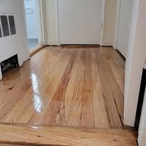Newly-finished, shiny wooden floor in a room with a white door and heater vent.
