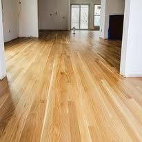 Wooden floorboards in a room, reflecting light. The floors are light brown.