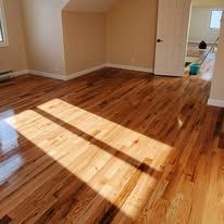 Hardwood floor, sunlit, empty room, light brown planks, shiny finish.