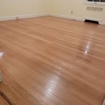 Newly finished light brown hardwood floor in an empty room, reflecting light.
