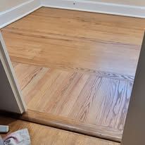 Light brown hardwood floor, with herringbone pattern and step down from doorway.