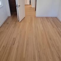 Light wood floor in a room, with a white wall and doorway.