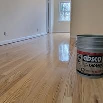 Close-up of a hardwood floor with a paint can on the right. A window is visible in the background.