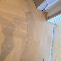 Wooden floor with curved line, light beige color, against white wall.