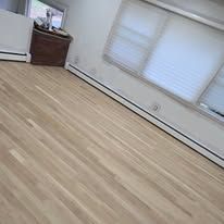 Light-colored hardwood floor in a room with a closed window and a small wooden cabinet.