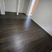 Dark hardwood floor in a room, partially lit by a window in the background.