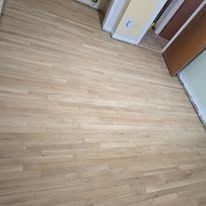 Light-colored hardwood floor in a room, angled view. Partially visible are doorways and walls.
