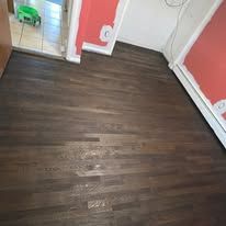 Dark stained hardwood floor. Red walls in the background. Open door in the corner with a green toy.