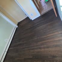 Dark wood flooring in a room with white trim, a pale yellow wall, and a partially visible white wall.