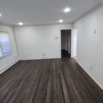 Empty room with dark hardwood floors, white walls, and a door on the right.