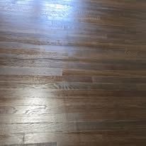 Wood flooring with visible grain and glossy finish. The color is brown and light reflects off the surface.