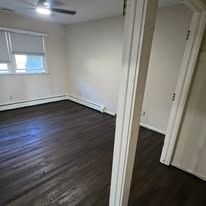 An empty room with dark wood flooring, a window, and a white door frame.