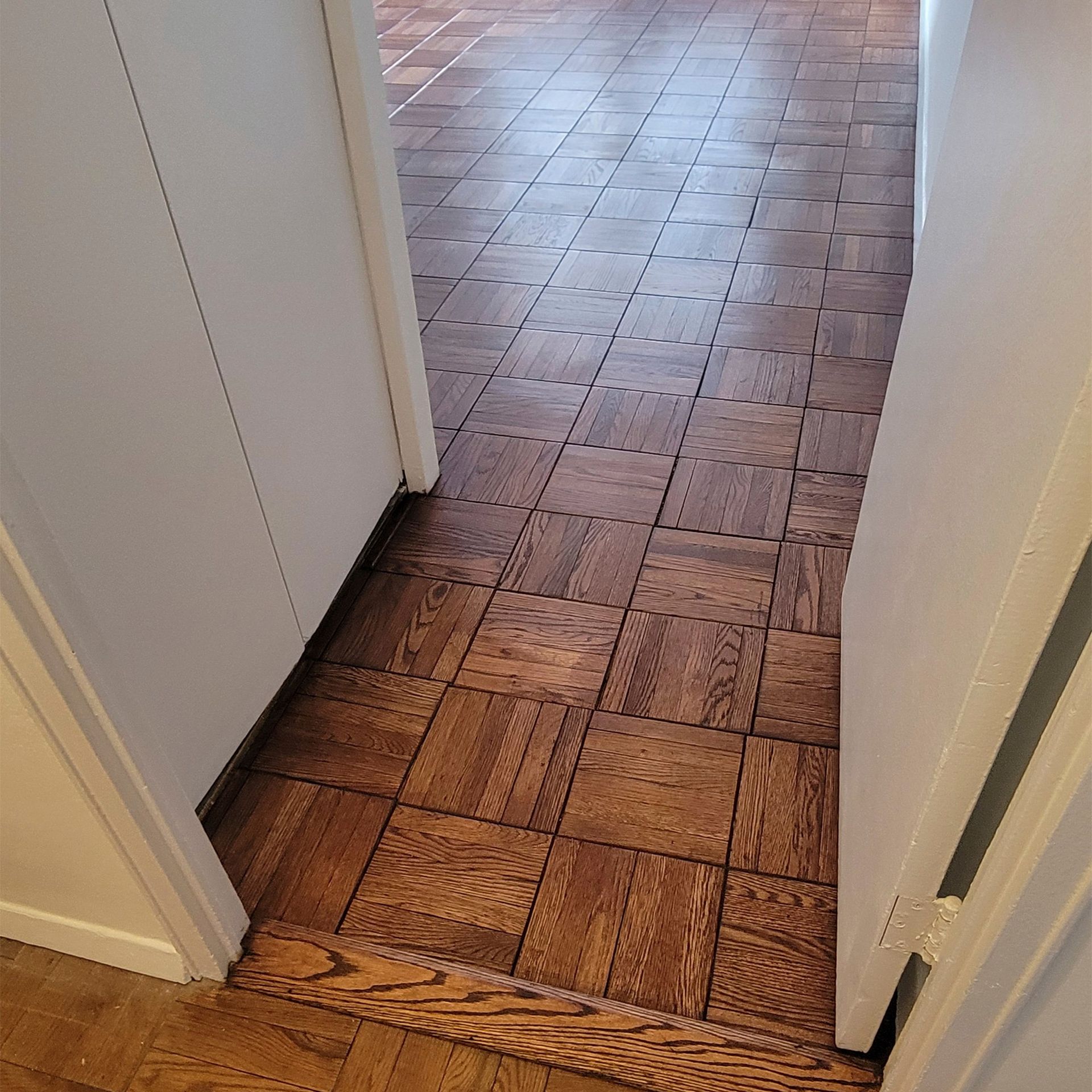 Wooden parquet flooring in a hallway, viewed between two white doorframes.