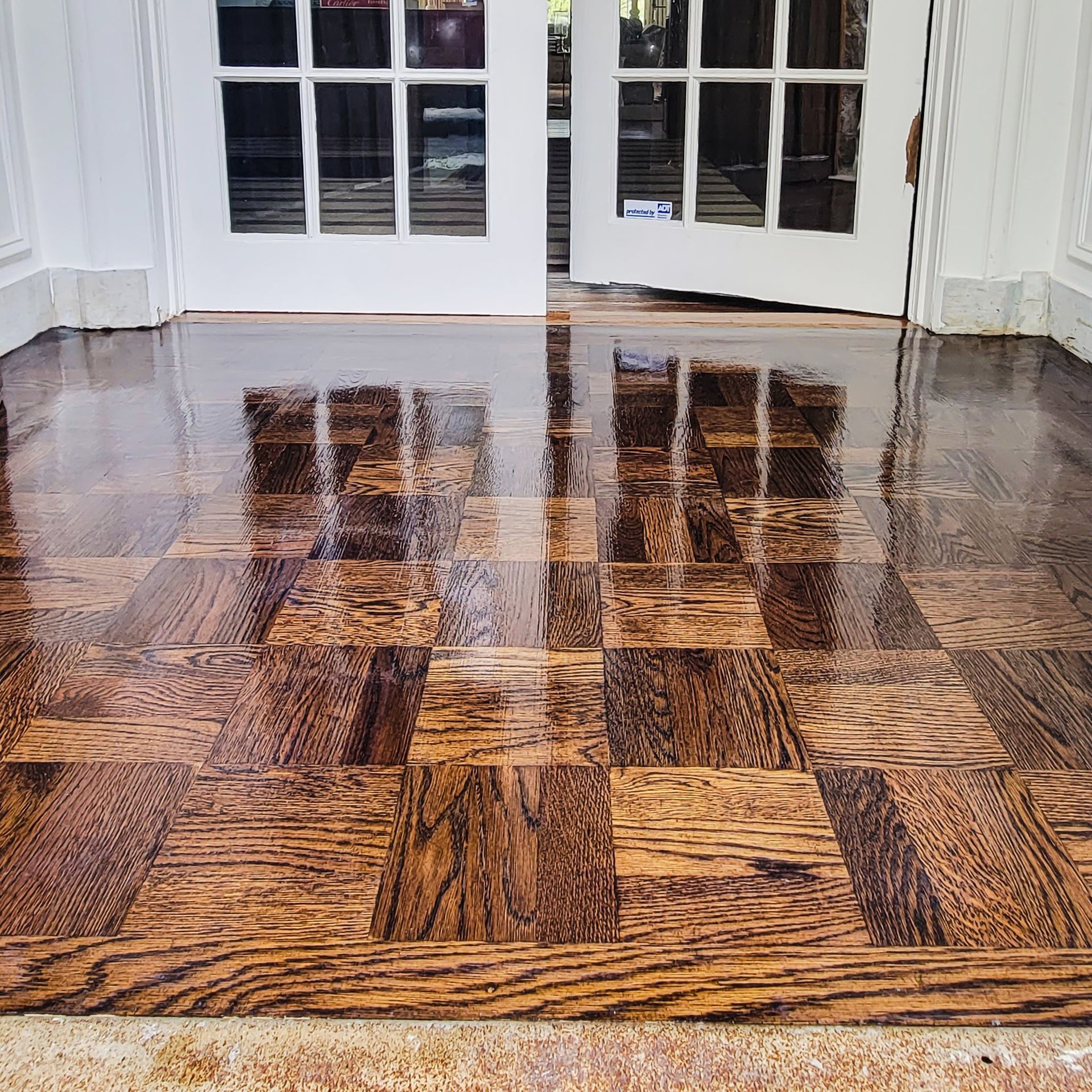 Shiny, dark wood parquet floor with reflections of white double doors.