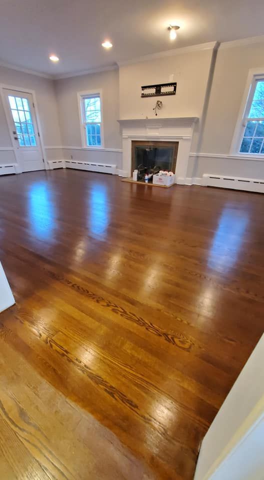 Newly refinished hardwood floor in a spacious living room with a fireplace and windows.