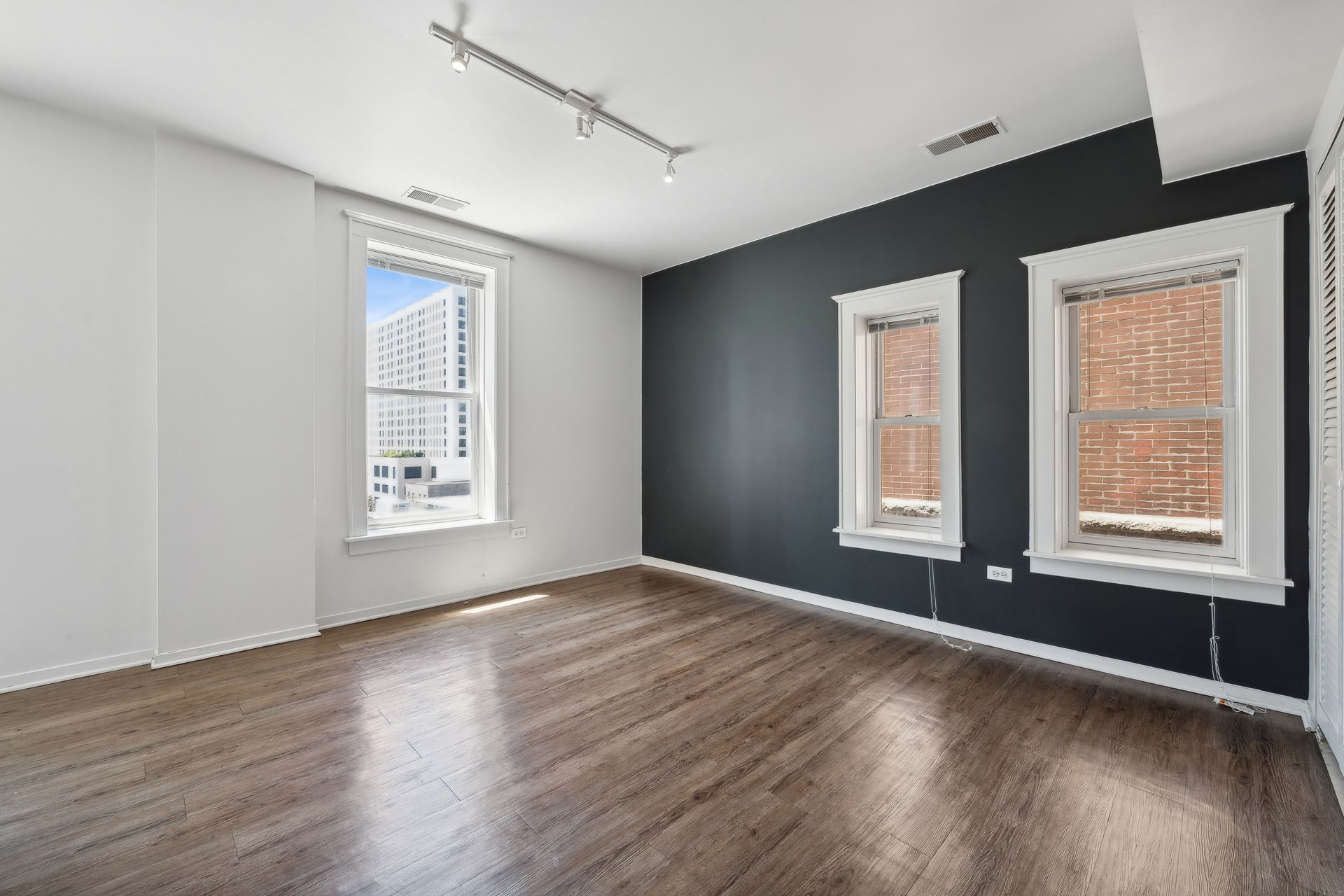 An empty living room with hardwood floors and two windows.