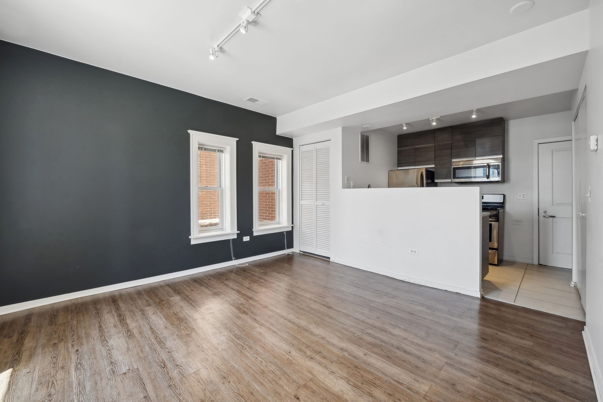 An empty living room with hardwood floors and a kitchen in the background.