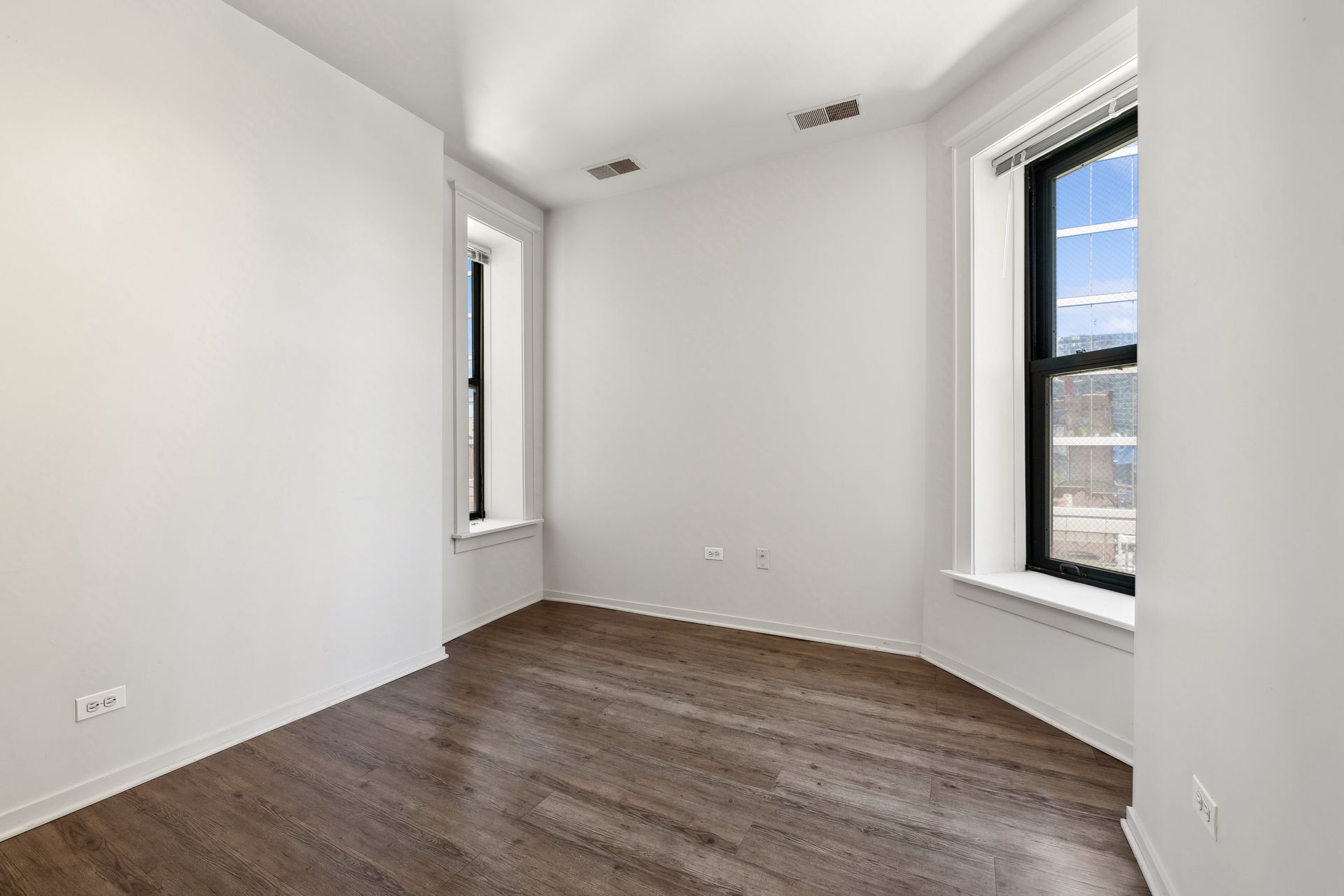 An empty room with hardwood floors and two windows.