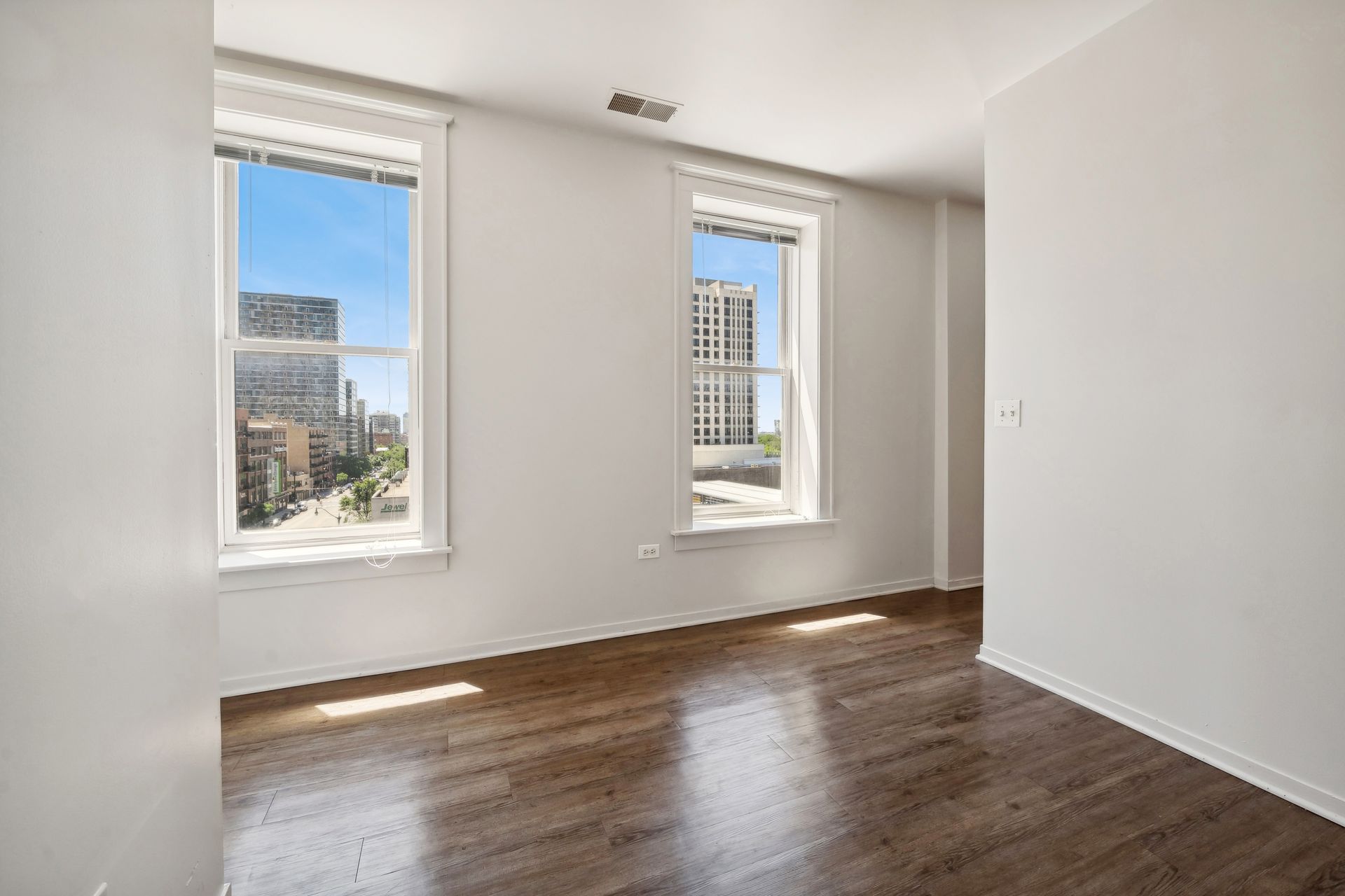 An empty room with hardwood floors and two windows.
