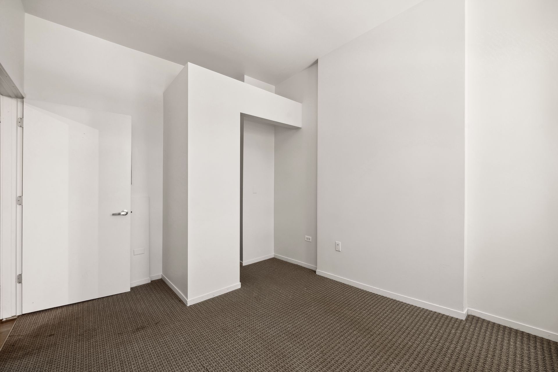 An empty room with a brown carpet and white walls.