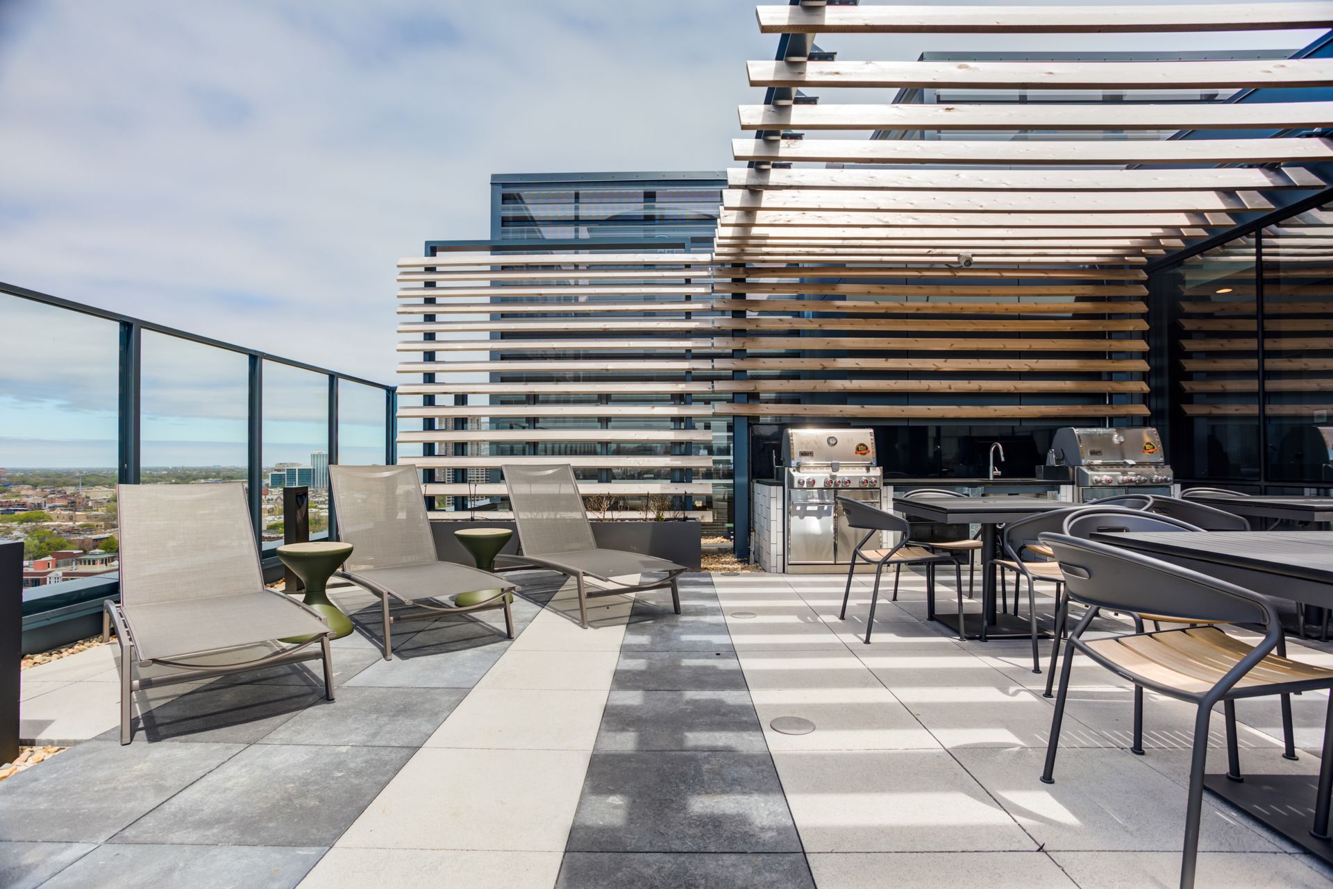A rooftop patio with chairs , tables and a grill.
