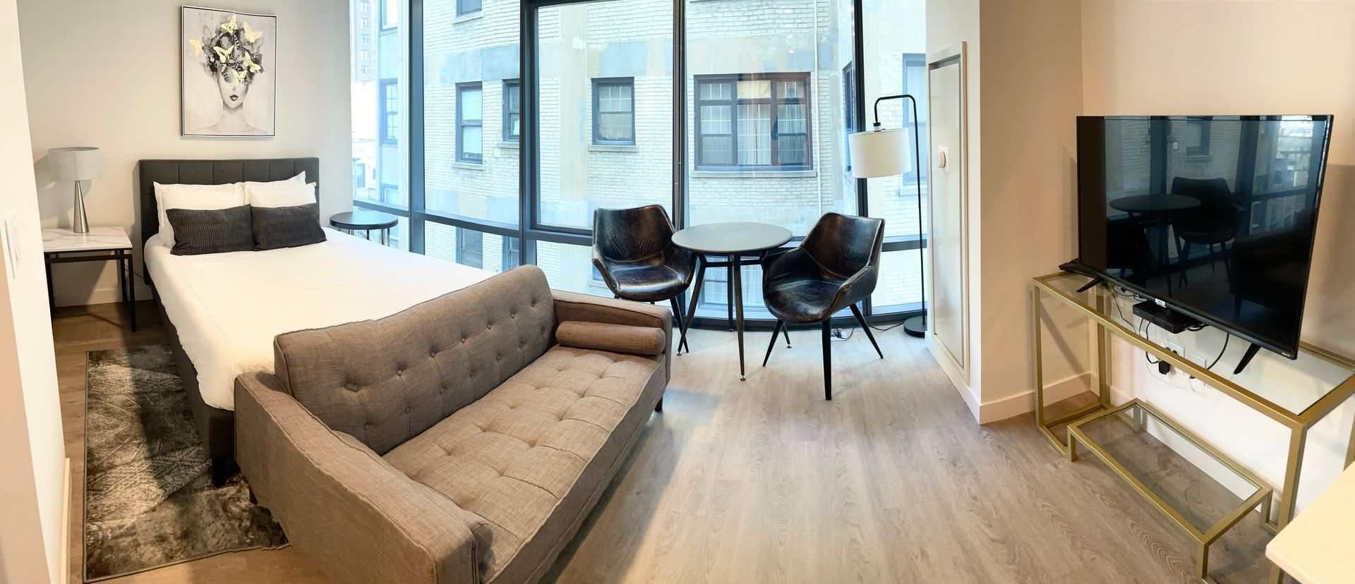 A bedroom with a bed , couch , television and large windows.