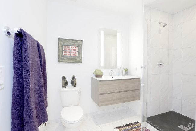 A bathroom with a toilet , sink , mirror and walk in shower.
