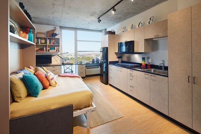 A bedroom with a bed and a kitchen in a small apartment.
