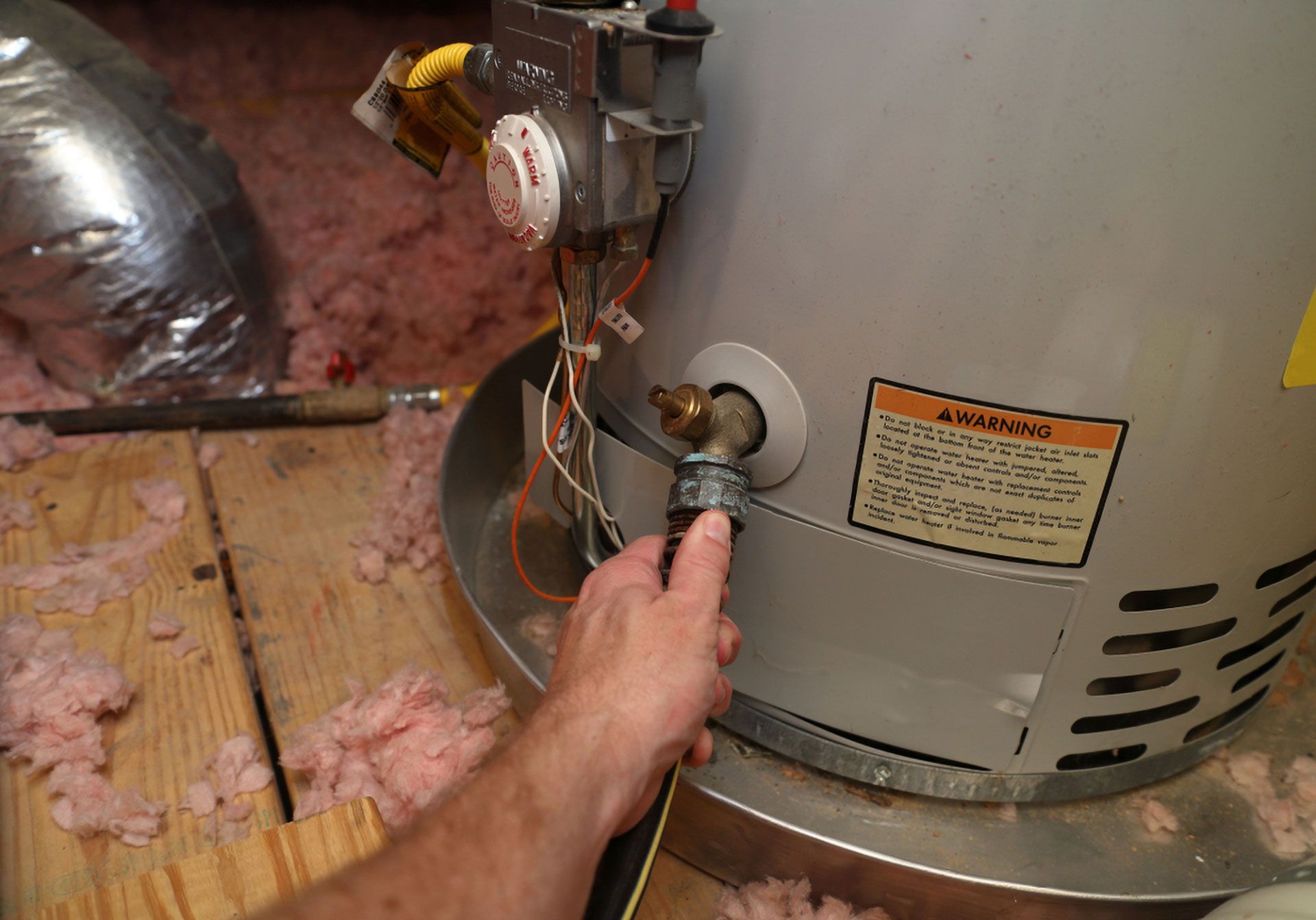Person Connecting a Hose to a Water Heater Drain Valve in an Attic — Full On Plumbing & Gas in Winnellie, NT