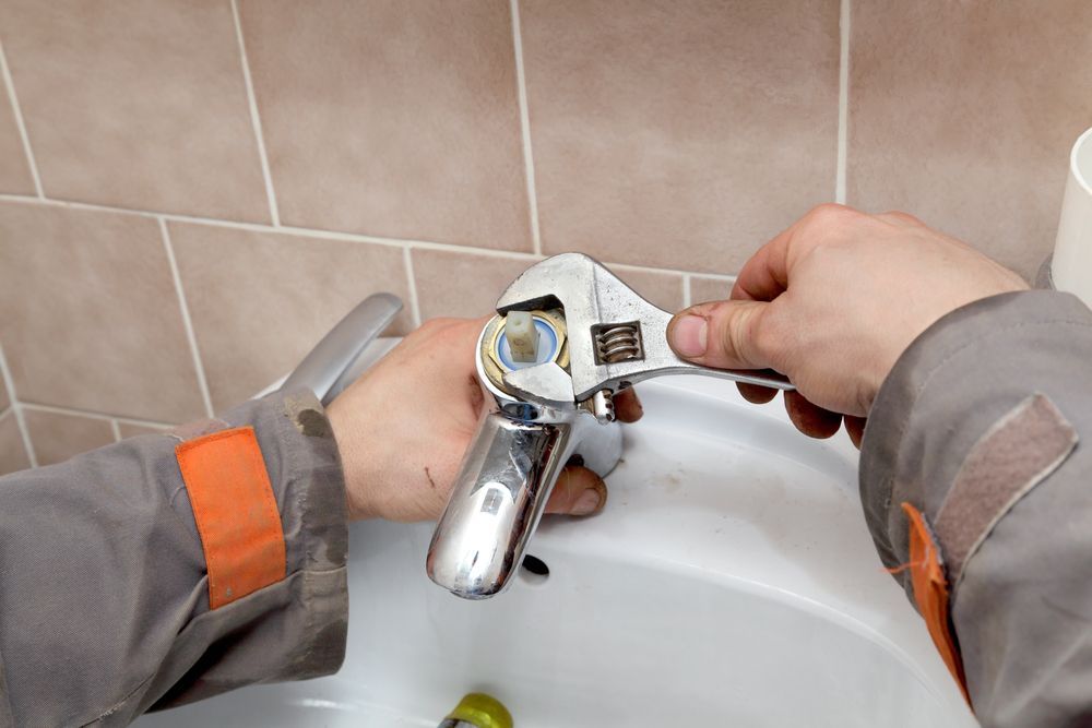 Person Using a Wrench to Repair a Faucet in a Bathroom With Beige Tiles — Full On Plumbing & Gas in Winnellie, NT