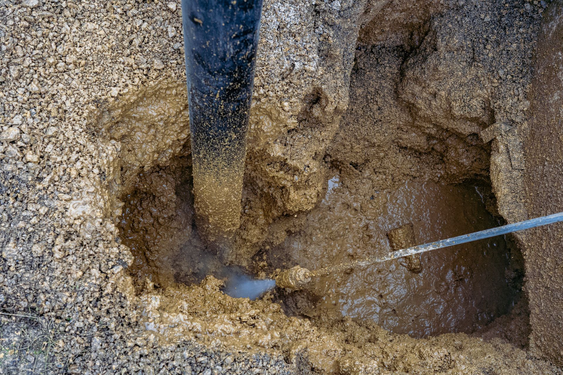 Black Pipe in a Hole in Gravel With Muddy Water and a Silver Rod — Full On Plumbing & Gas in Parap, NT