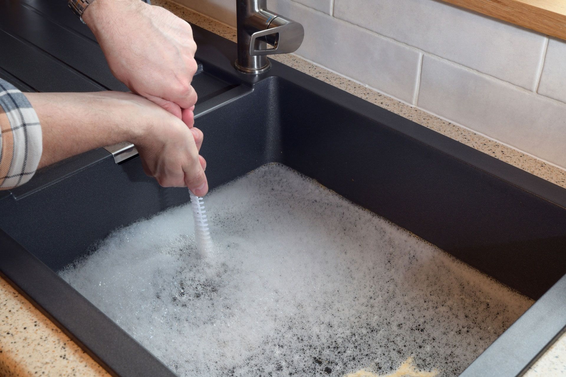 Person Using a Plunger in a Dark Gray Kitchen Sink Filled With Soapy Water — Full On Plumbing & Gas in Winnellie, NT