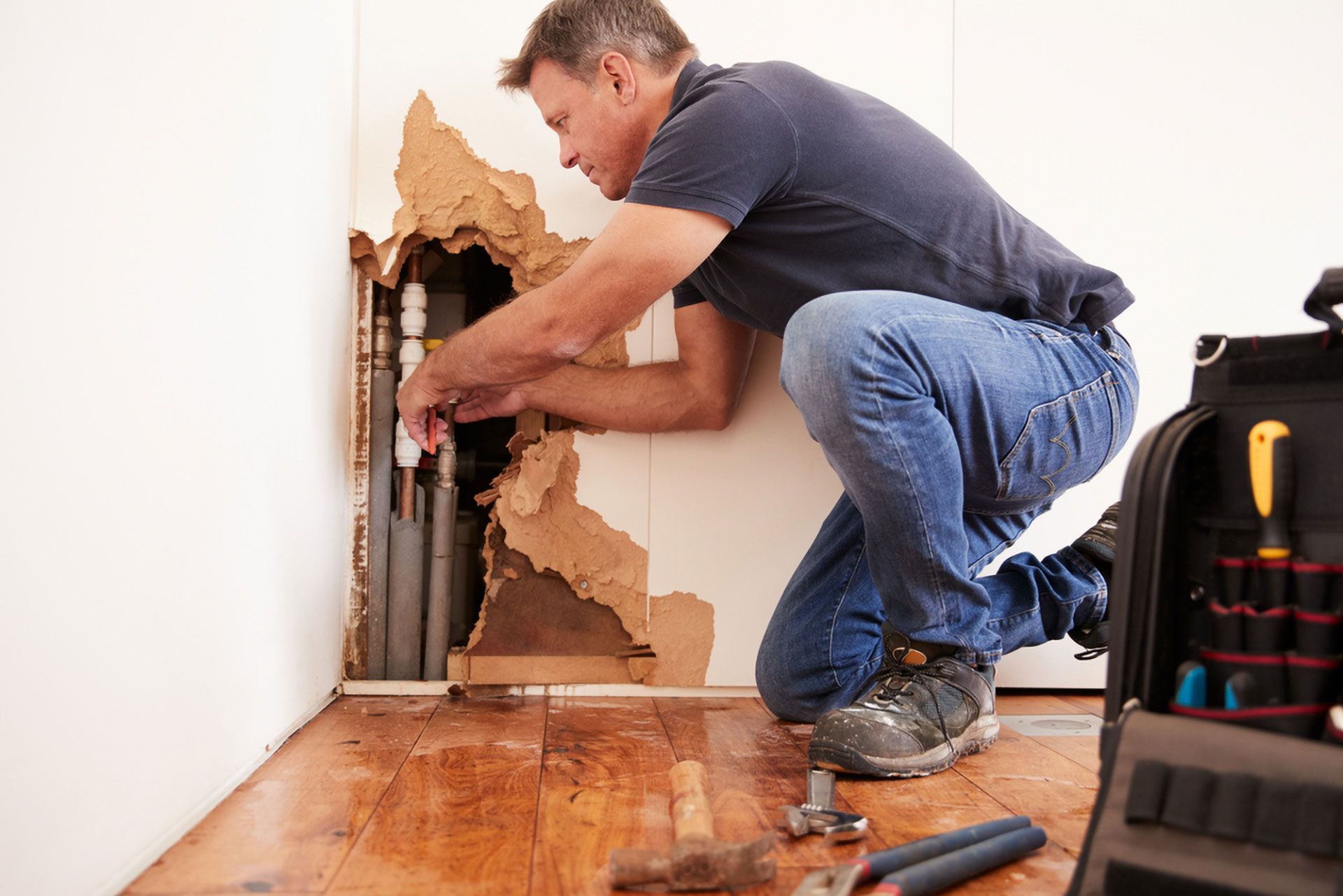 Plumber Kneeling, Repairing Pipes Behind a Damaged Wall in a Home — Full On Plumbing & Gas in Winnellie, NT