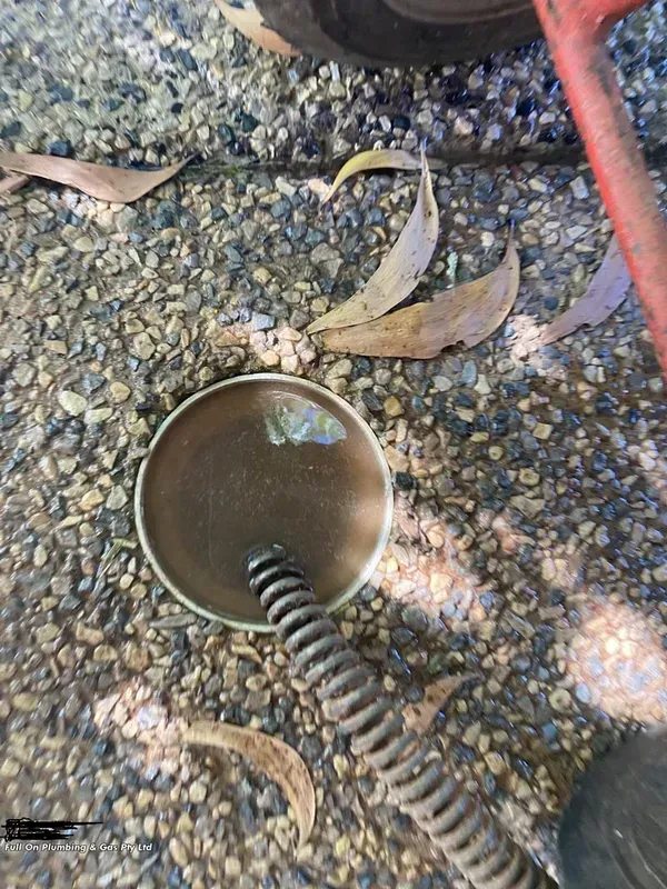 A Drain With a Cable Inserted is Surrounded by Gravel and Leaves — Full On Plumbing & Gas in Winnellie, NT
