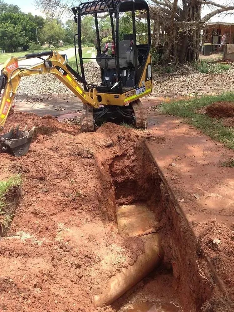 Yellow Excavator Digging a Trench, Exposing a Pipe in Reddish Soil — Full On Plumbing & Gas in Winnellie, NT