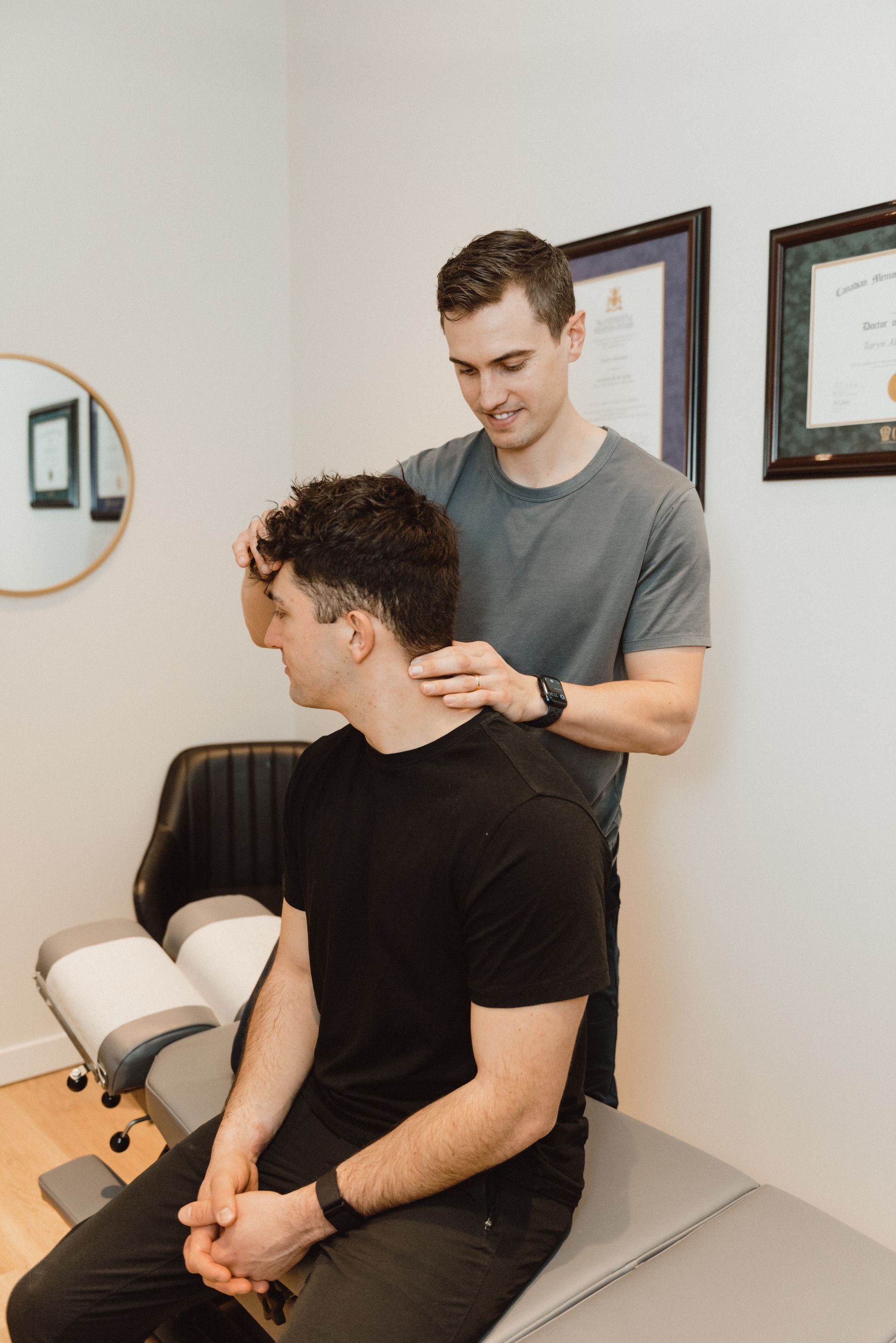 A man is sitting on a table while a doctor examines his neck.