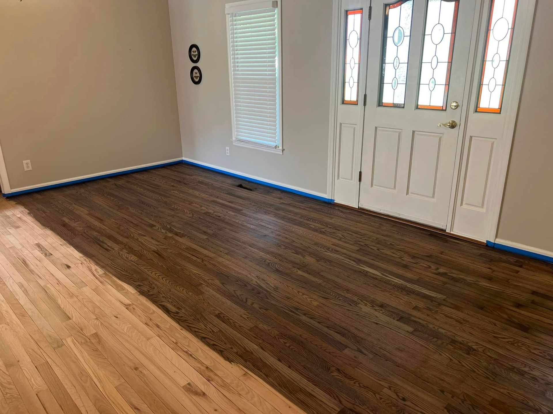 Wood floor half stained brown, half unstained. Interior view with a door and window.