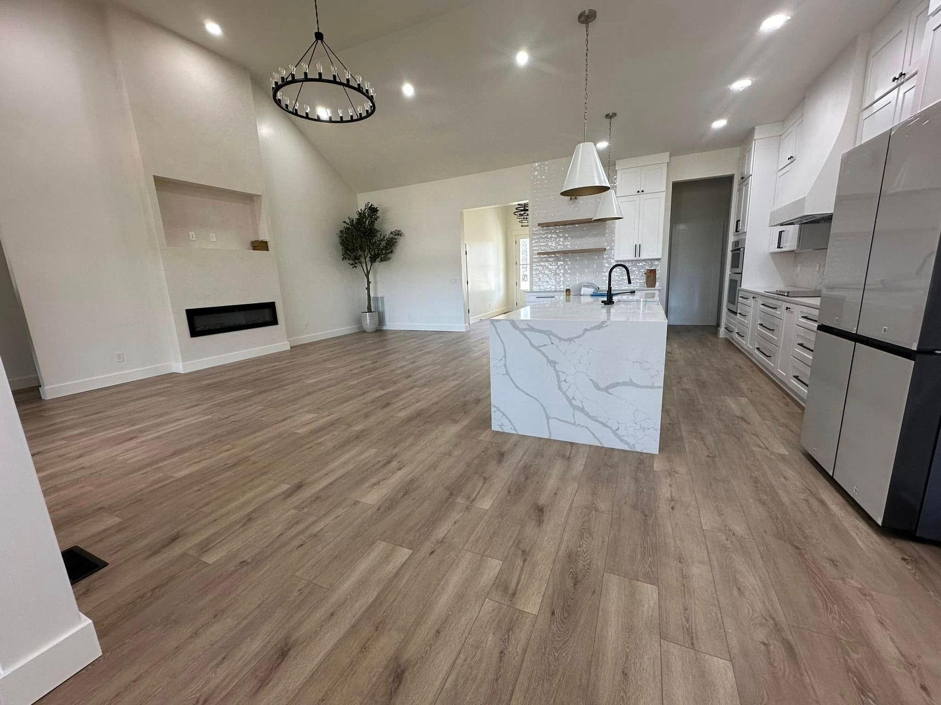 Modern kitchen and living area with white walls, wood floors, and a kitchen island.