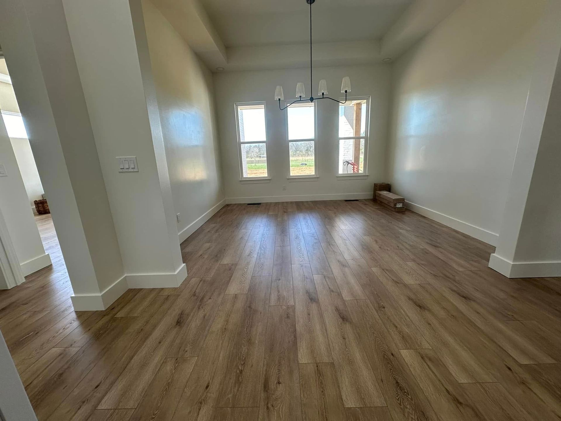 Empty dining room with wood floors, three windows, and a chandelier. White walls and trim.