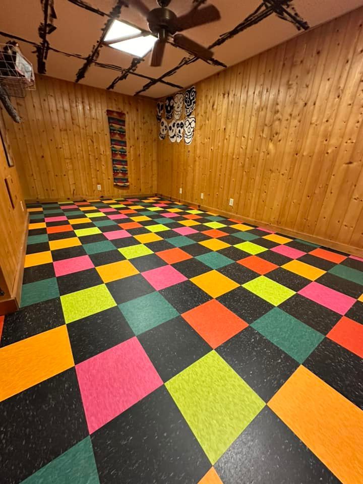 Room with checkerboard floor of bright colors, wood-paneled walls, and a ceiling fan.