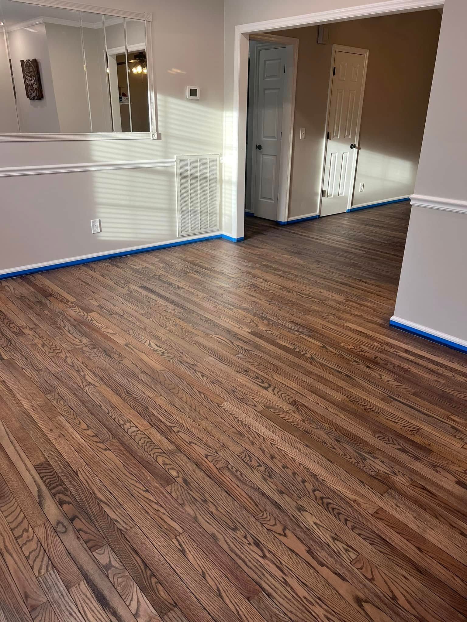 Dark stained hardwood floors in a room, blue painter's tape along the baseboards. Doorways in background.