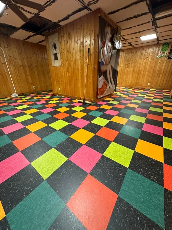 Room with colorful checkered floor and wood panel walls. A machine is on the wall.