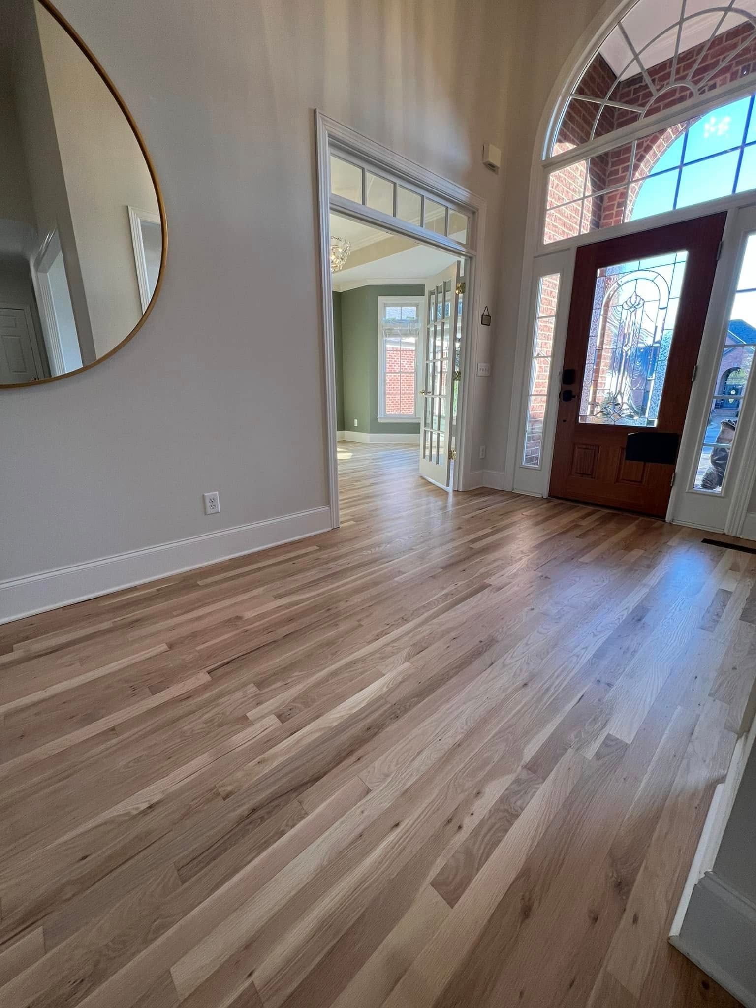Wooden floor of an entryway with a round mirror, door, and arched window.
