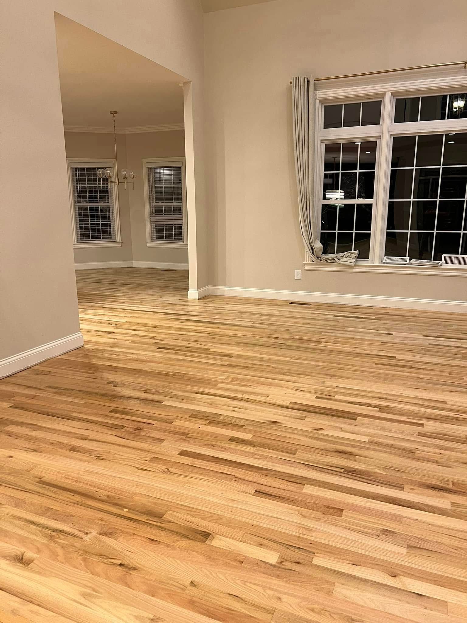 Light wood floors in a mostly empty room with beige walls and windows with white frames.