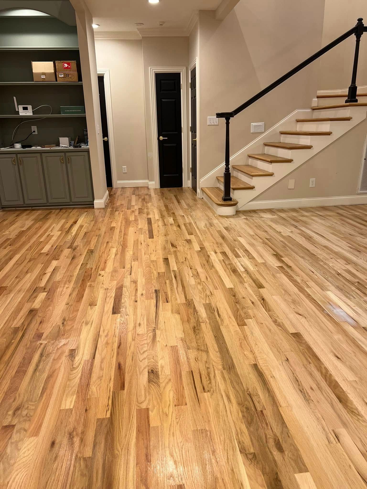 Hardwood floors in a house. Staircase with black railing, beige walls, and gray cabinets.