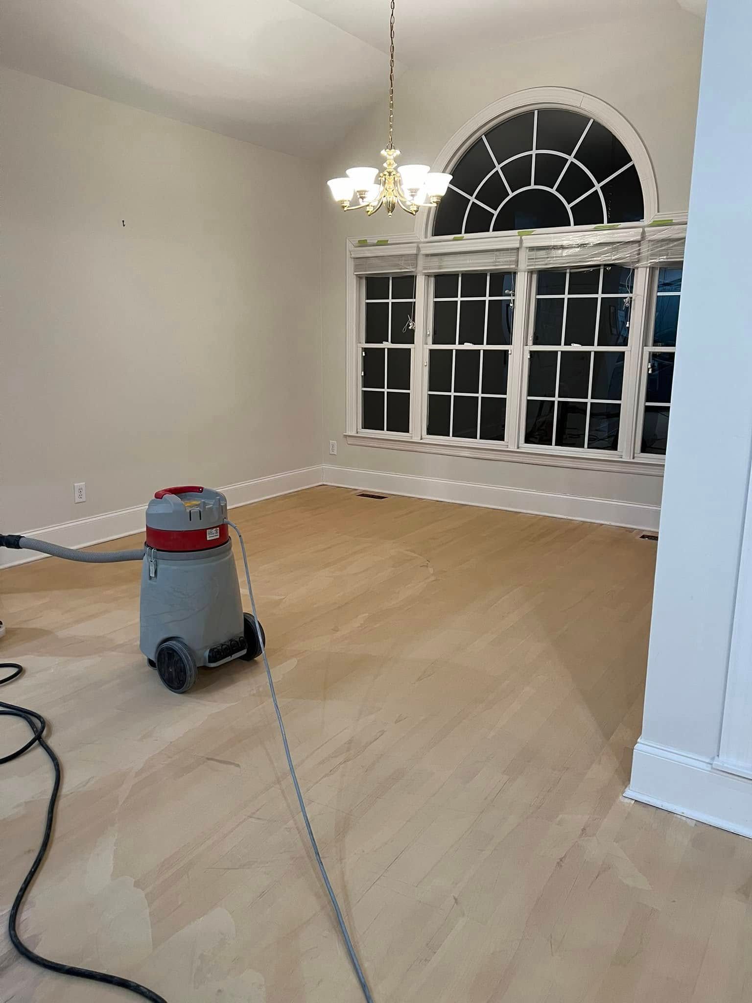 Room with bare wood floor, vacuum cleaner, and large arched window. White walls and trim.