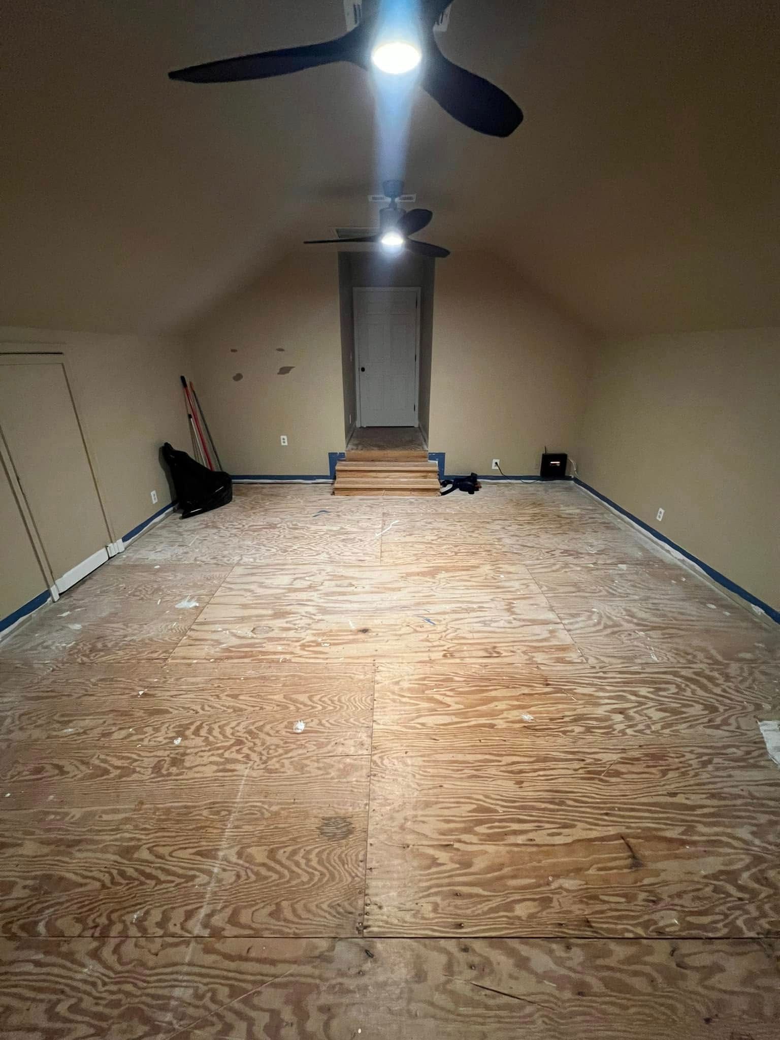 Empty attic room with wooden floor, sloped ceiling, and doorway in the back.