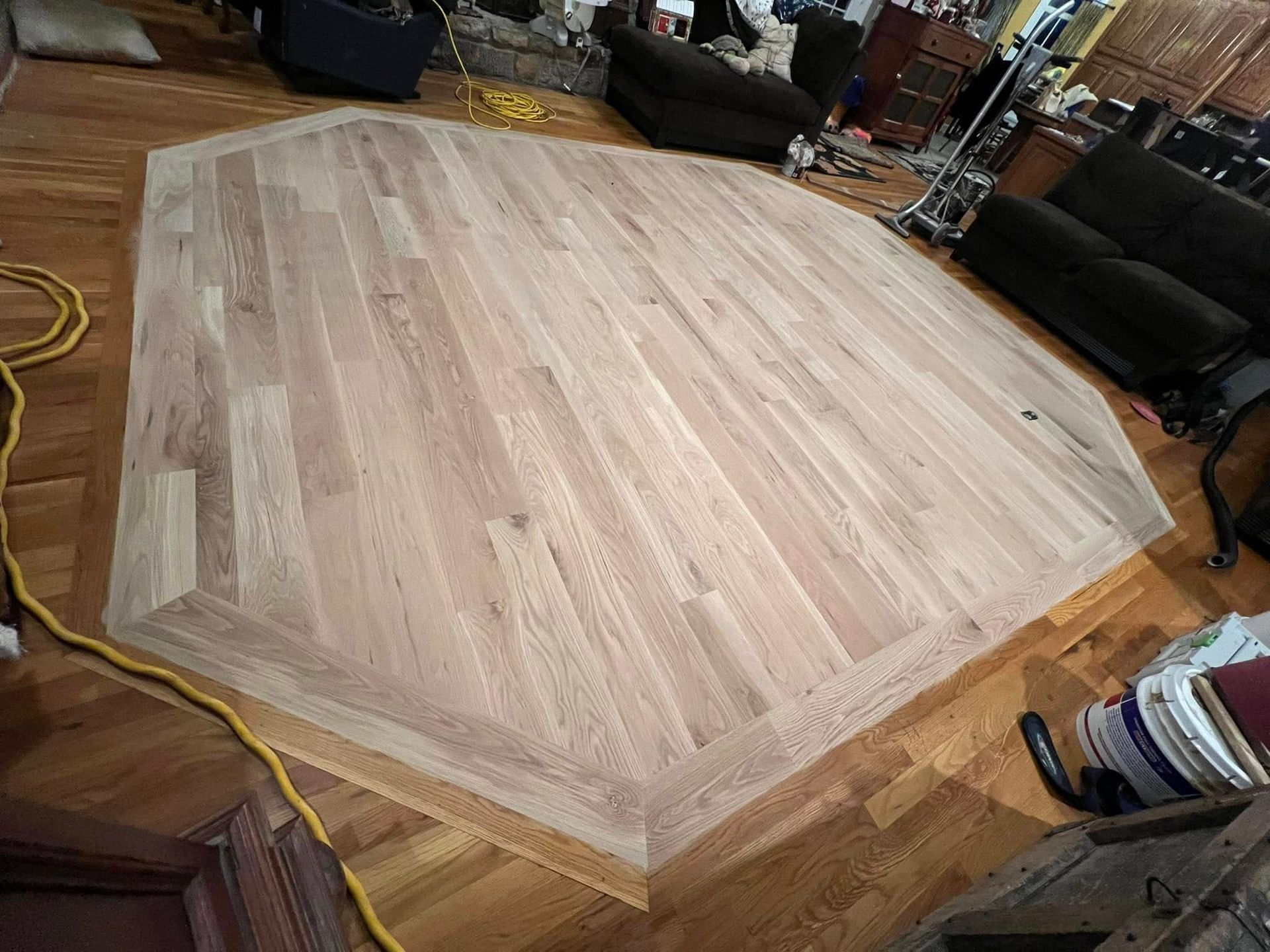 Newly installed light-colored wooden floor in an octagonal shape, surrounded by older wooden flooring.