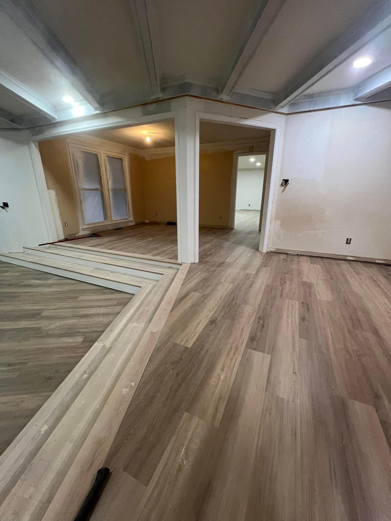 Interior view of a room under renovation, featuring new flooring and exposed framing.