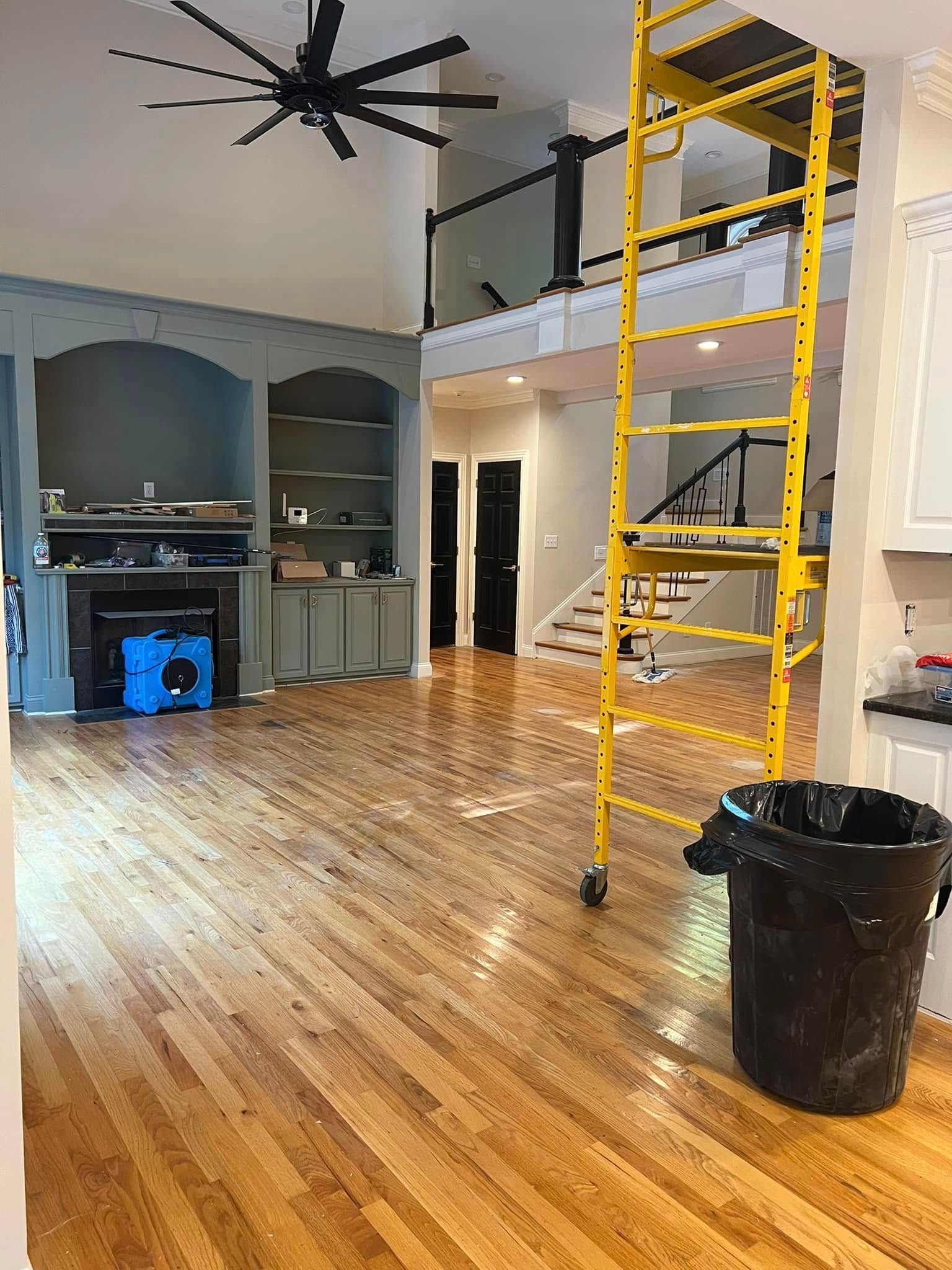 Interior view of a house undergoing renovations. Yellow scaffold, hardwood floors, built-in shelving and fireplace.